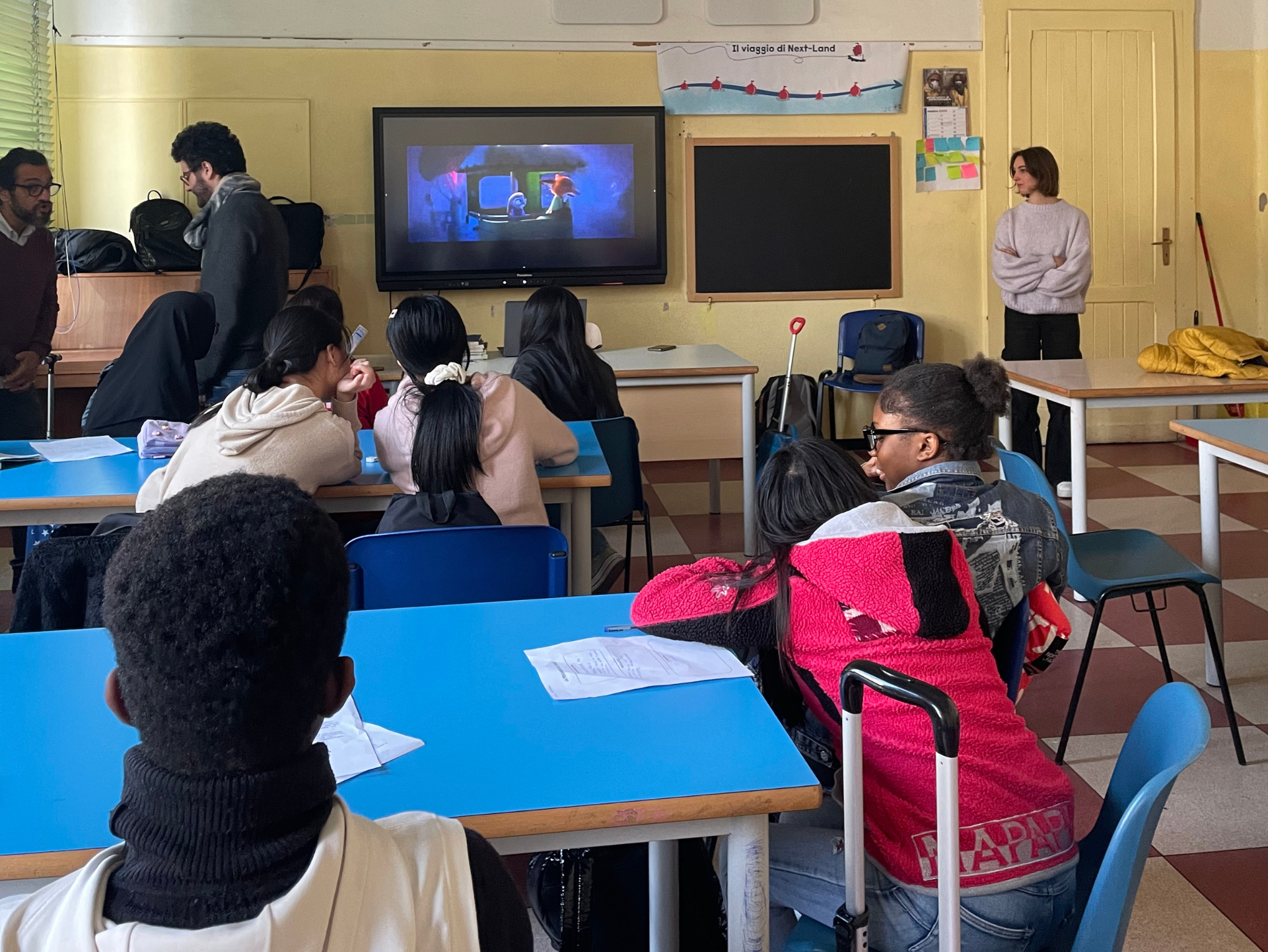 Copertina del laboratorio "La discriminazione cos'è?" raffigurativa di un gruppo di studenti e studentesse in età adolescenziale di diverso background culturale in una classe, di spalle che guardano un film