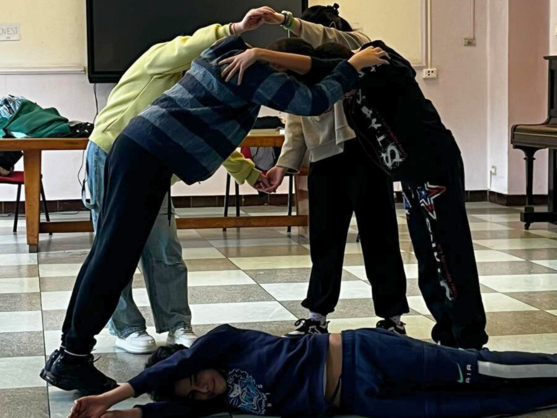 Copertina del laboratorio Torneo di Improvvisazione teatrale raffigurante un gruppo di studenti e studentesse tra i 11 e i 13 anni che in classe improvvisano un pezzo teatrale, un ragazzo è sdraiato a terra mentre un gruppo di ragazzi si abbraccia formando un arco