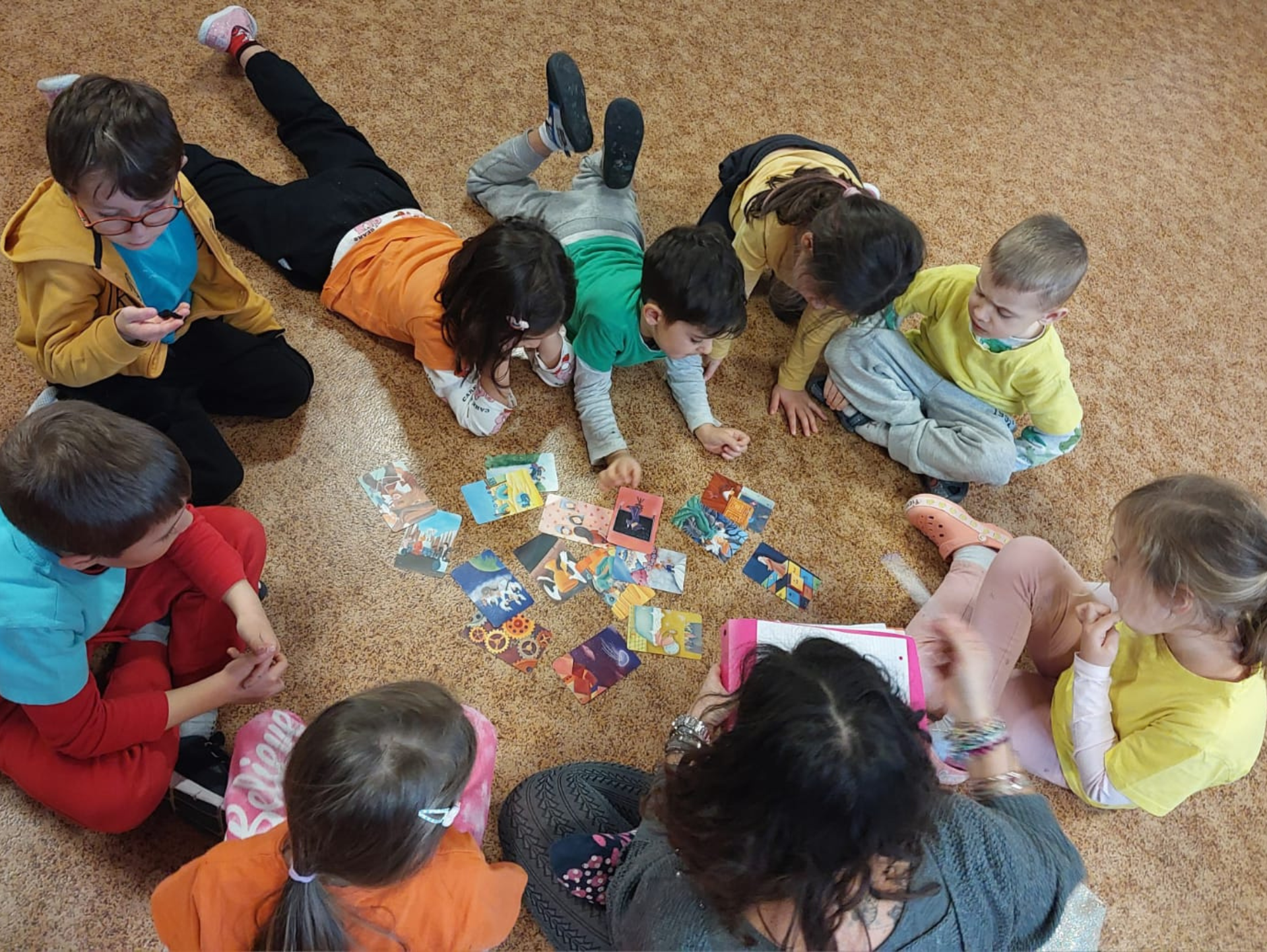 Copertina del laboratorio Prime regole per bambine/i e famiglie rappresentativo di un gruppo di bambine/i attorno a delle carte da gioco, che giocano seduti a terra